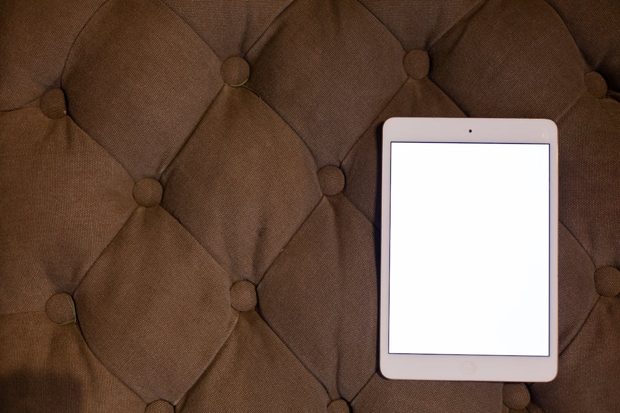 A blank tablet on a brown tufted cushion, perfect for mockup or design presentation.